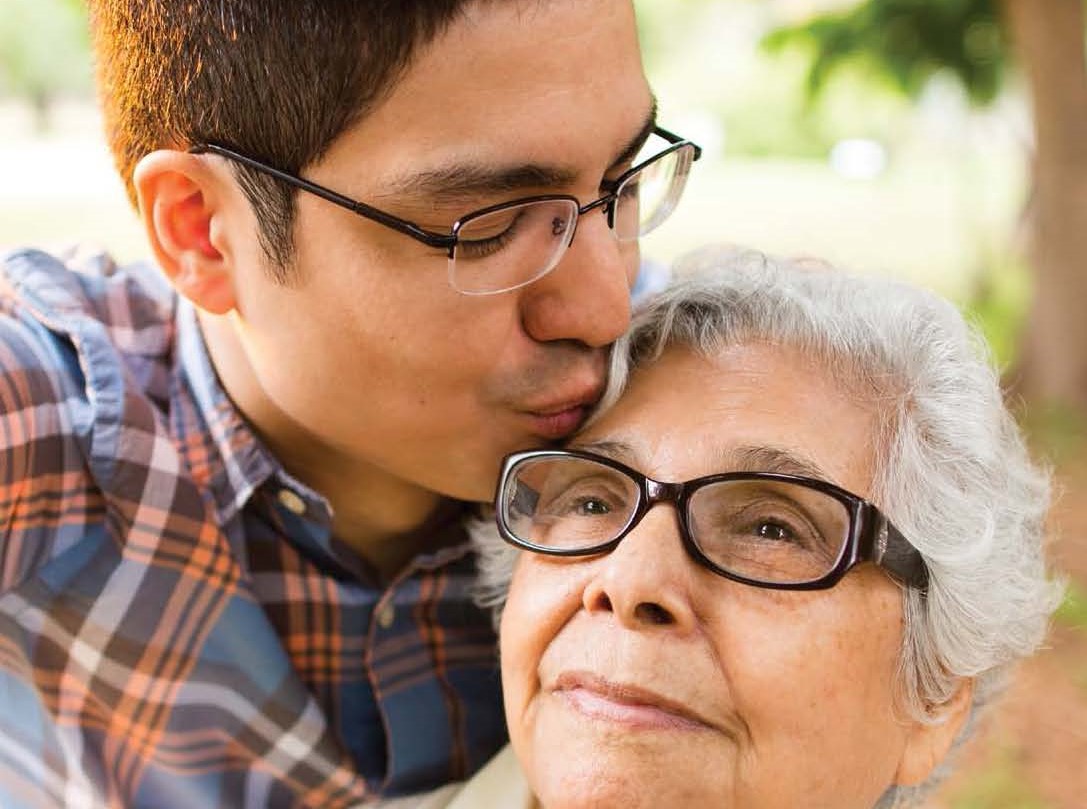 Latinx son kissing mother's forehead; caregiving